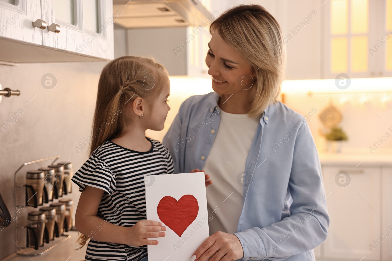 Photo of Little daughter congratulating her mom with greeting card in kitchen. Happy Mother's Day