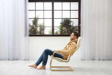 Photo of Attractive man relaxing in armchair near window at home