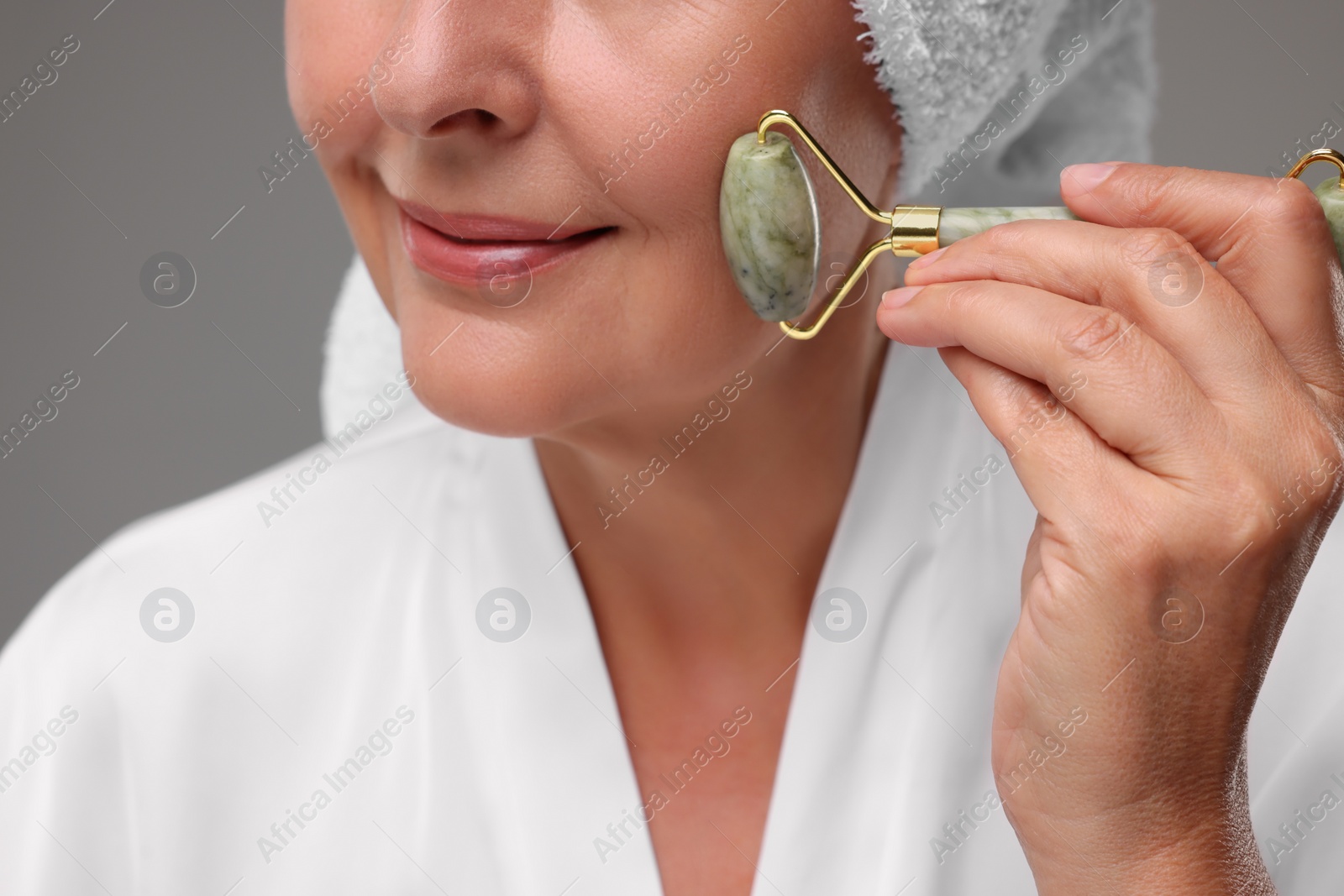 Photo of Woman massaging her face with jade roller on grey background, closeup