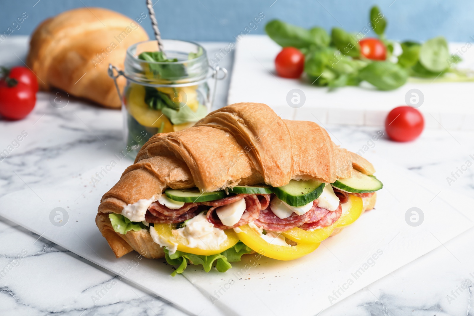 Photo of Tasty croissant sandwich with salami on table