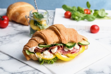 Photo of Tasty croissant sandwich with salami on table