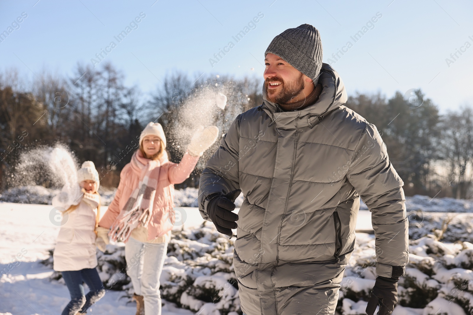 Photo of Portrait of smiling man and his family playing snowballs in winter park