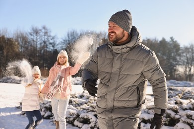 Photo of Portrait of smiling man and his family playing snowballs in winter park