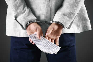 Photo of Man in handcuffs holding bribe money on dark background, closeup