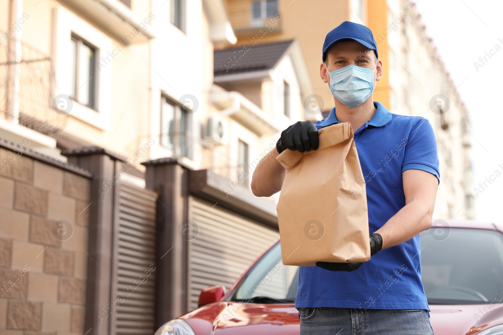 Photo of Courier in protective mask and gloves with order near car outdoors. Food delivery service during coronavirus quarantine