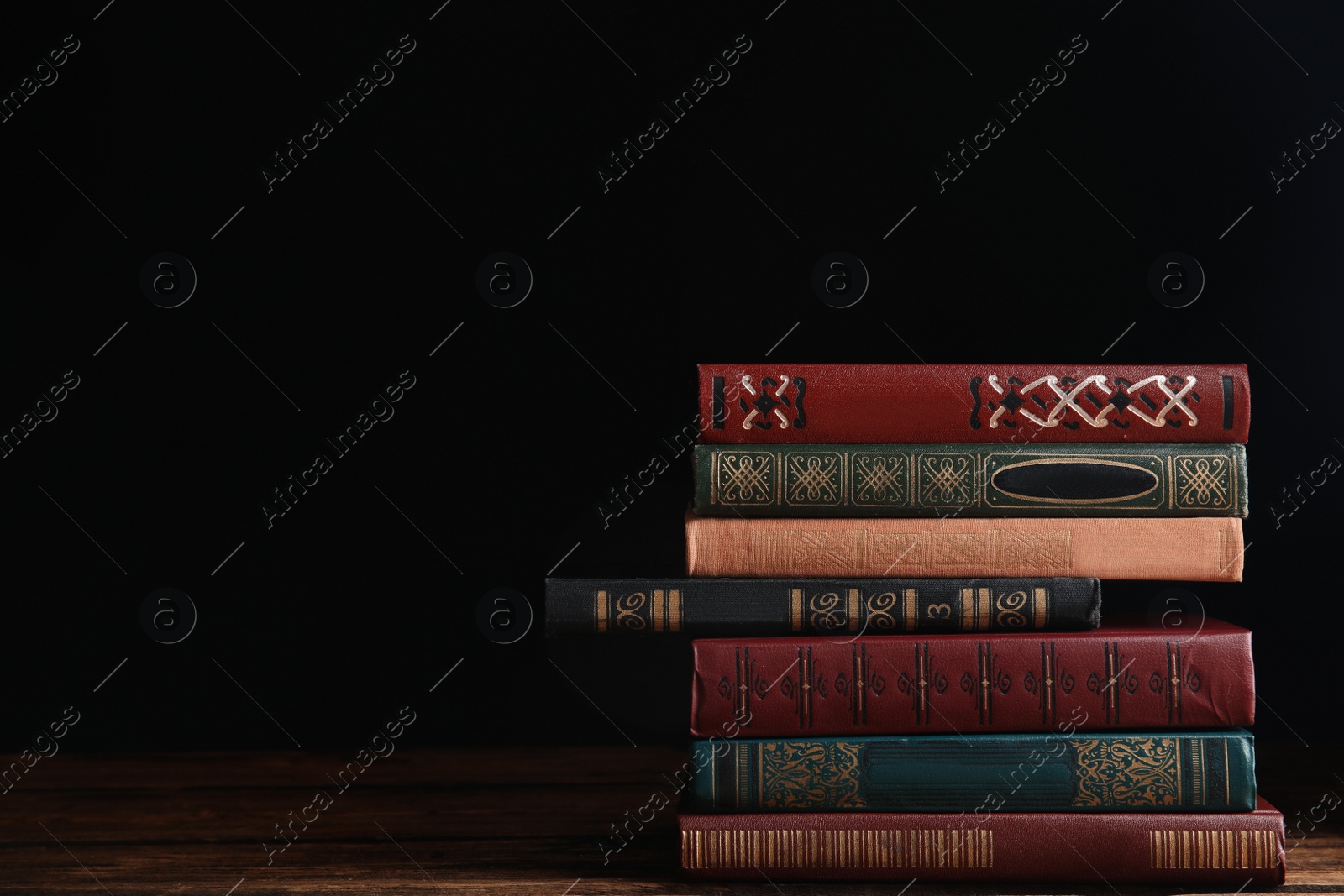 Photo of Collection of different books on wooden table against dark background. Space for text