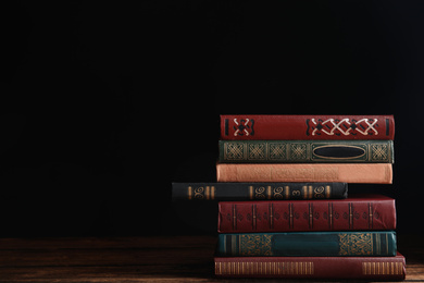 Photo of Collection of different books on wooden table against dark background. Space for text