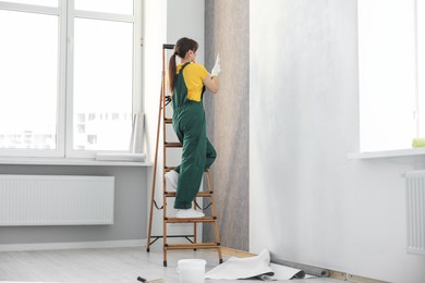 Woman hanging stylish gray wallpaper in room