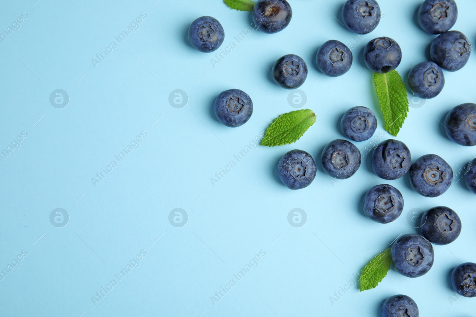 Photo of Tasty ripe blueberries and leaves on blue background, flat lay with space for text