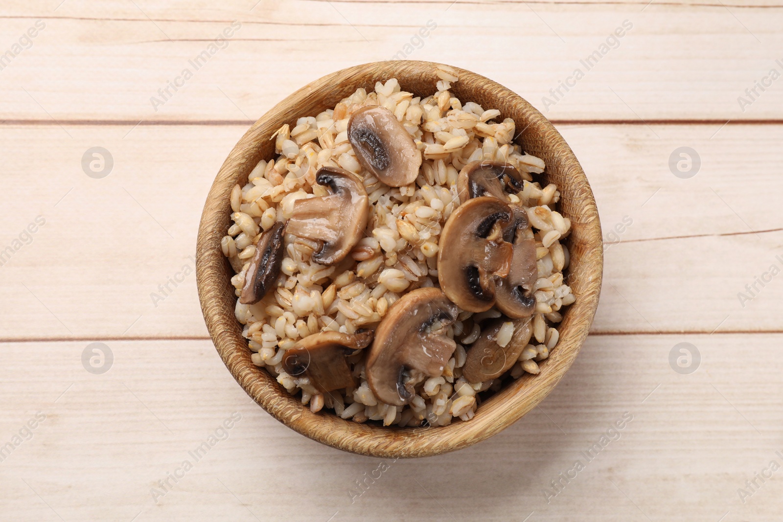 Photo of Delicious pearl barley with mushrooms in bowl on. wooden table, top view