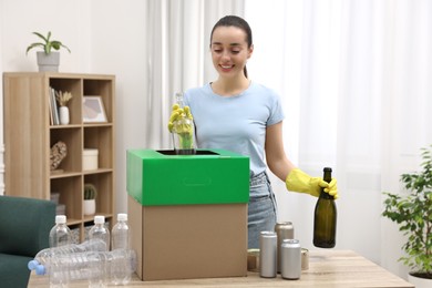 Garbage sorting. Smiling woman throwing glass bottle into cardboard box in room