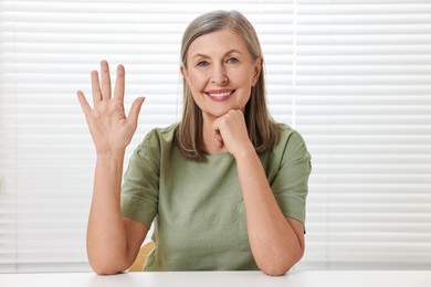 Happy woman waving hello at white table indoors