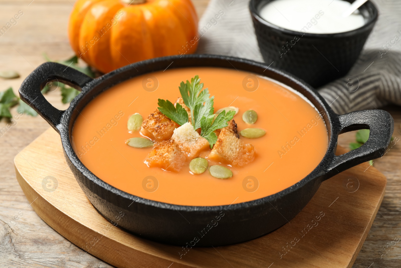 Photo of Tasty creamy pumpkin soup with croutons, seeds and parsley in bowl on wooden table