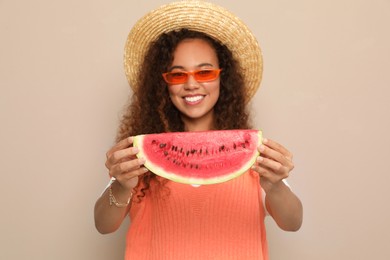 Photo of Beautiful young African American woman with slice of watermelon against beige background, focus on hands
