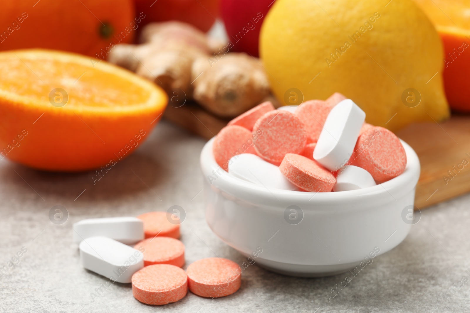 Photo of Dietary supplements. Different pills in bowl, fruits and ginger on grey table, closeup