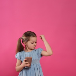 Photo of Cute little child with glass of tasty chocolate milk on pink background, space for text