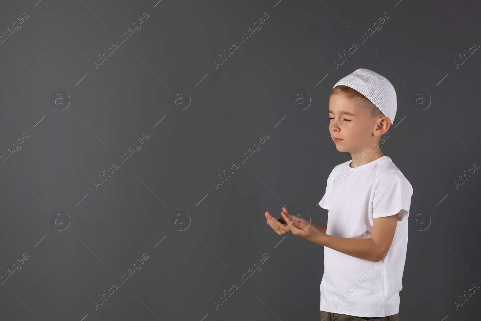 Photo of Little Muslim boy praying on gray background. Space for text