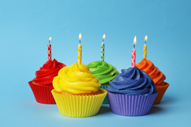 Photo of Delicious birthday cupcakes with burning candles on light blue background