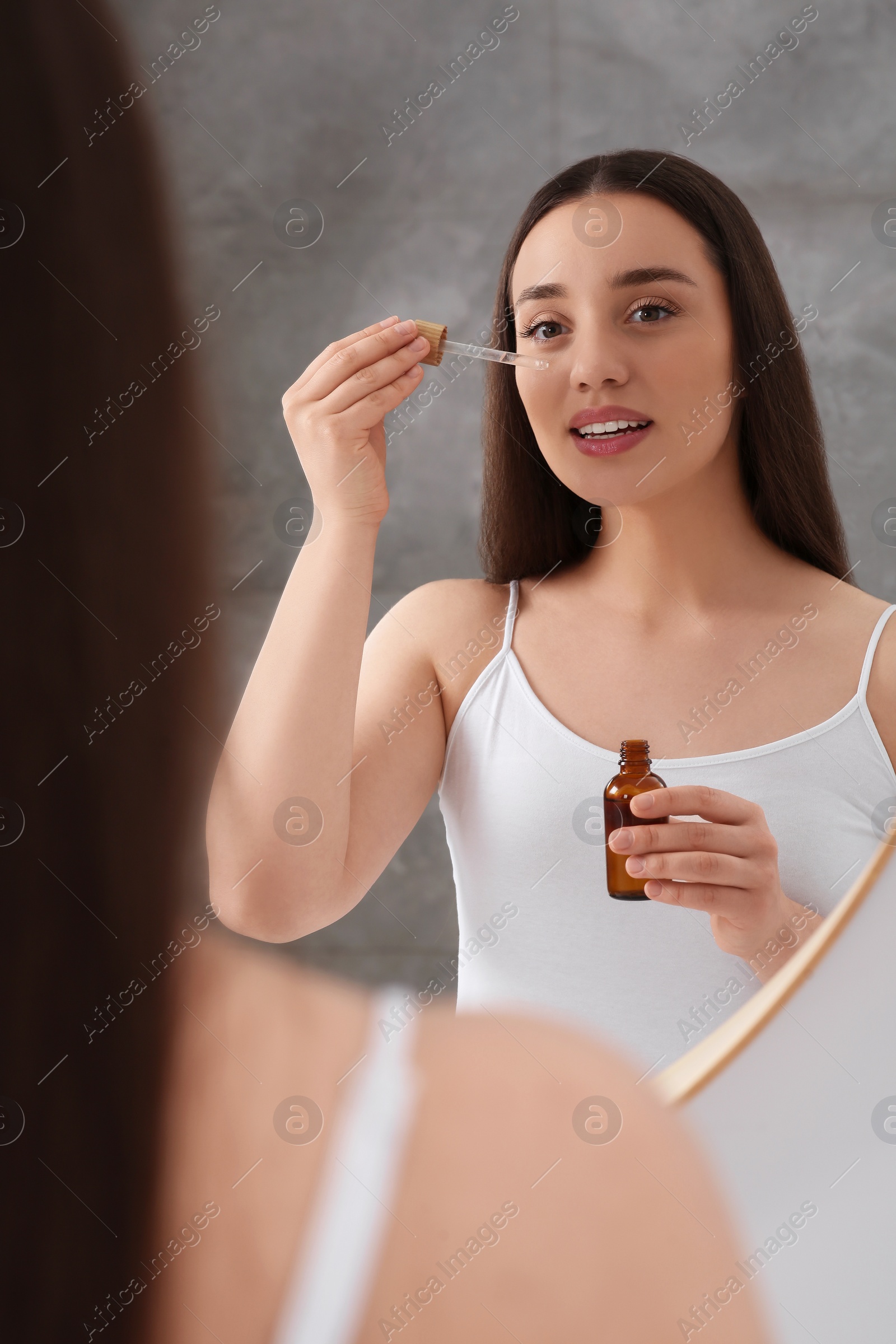 Photo of Woman applying essential oil onto face near mirror