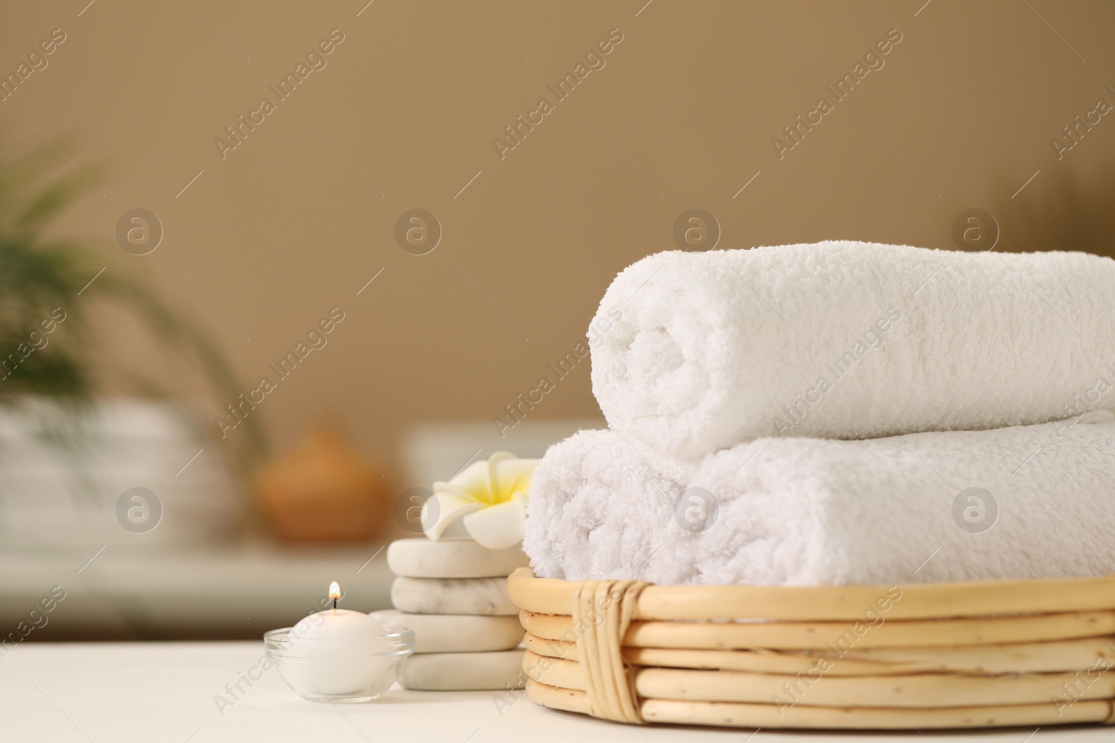 Photo of Spa composition. Rolled towels, massage stones, burning candle and plumeria flower on table. Space for text