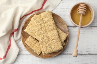 Board with tasty sesame kozinaki bars and honey on white wooden table, flat lay