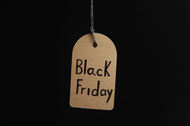 Photo of Tag with words BLACK FRIDAY hanging on dark background