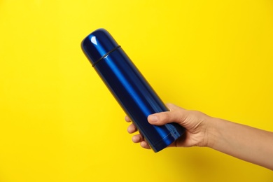 Woman holding modern blue thermos on yellow background, closeup