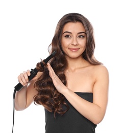 Beautiful woman using curler on her shiny wavy hair against white background