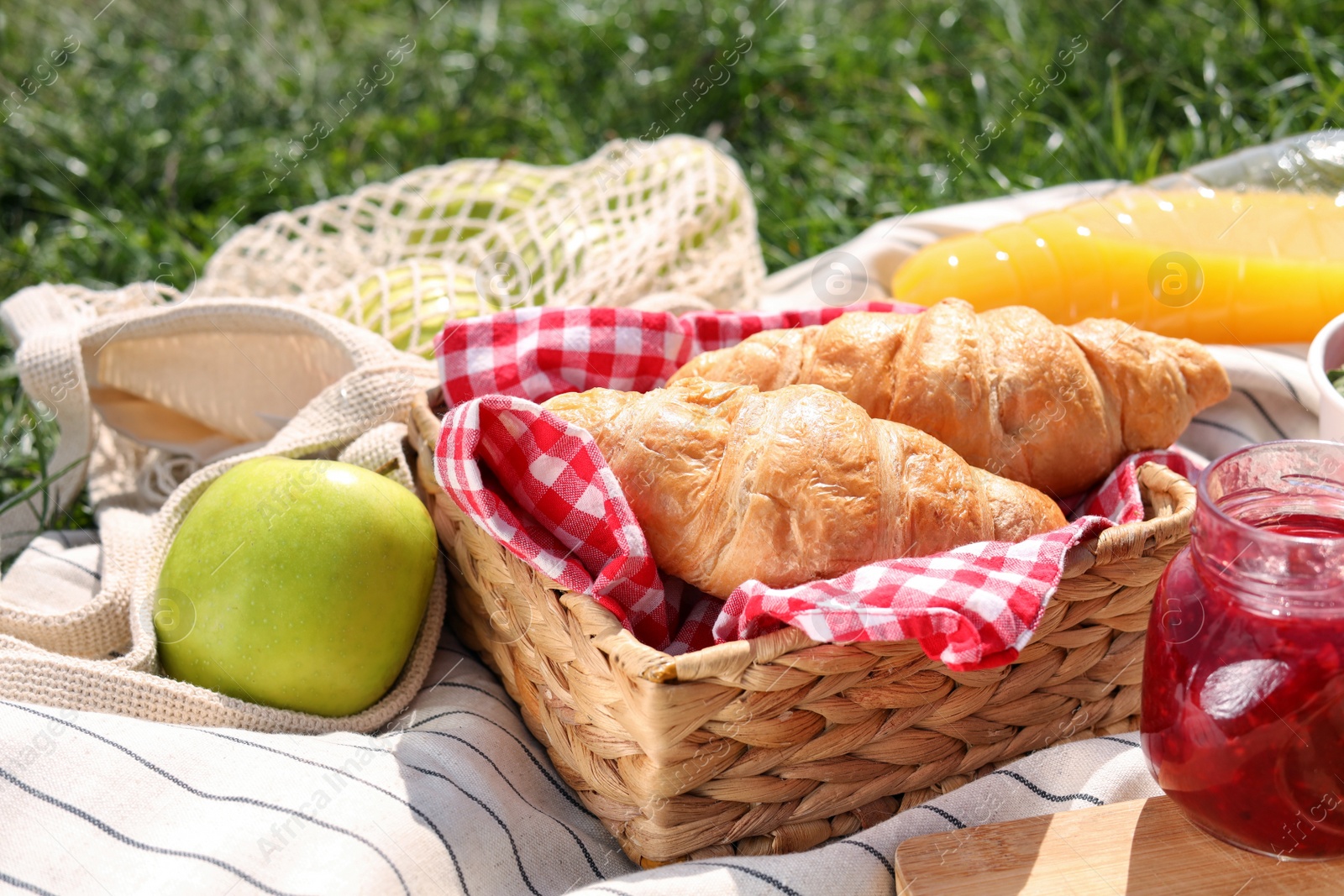 Photo of Jar of jam, croissants and apple on blanket outdoors. Summer picnic