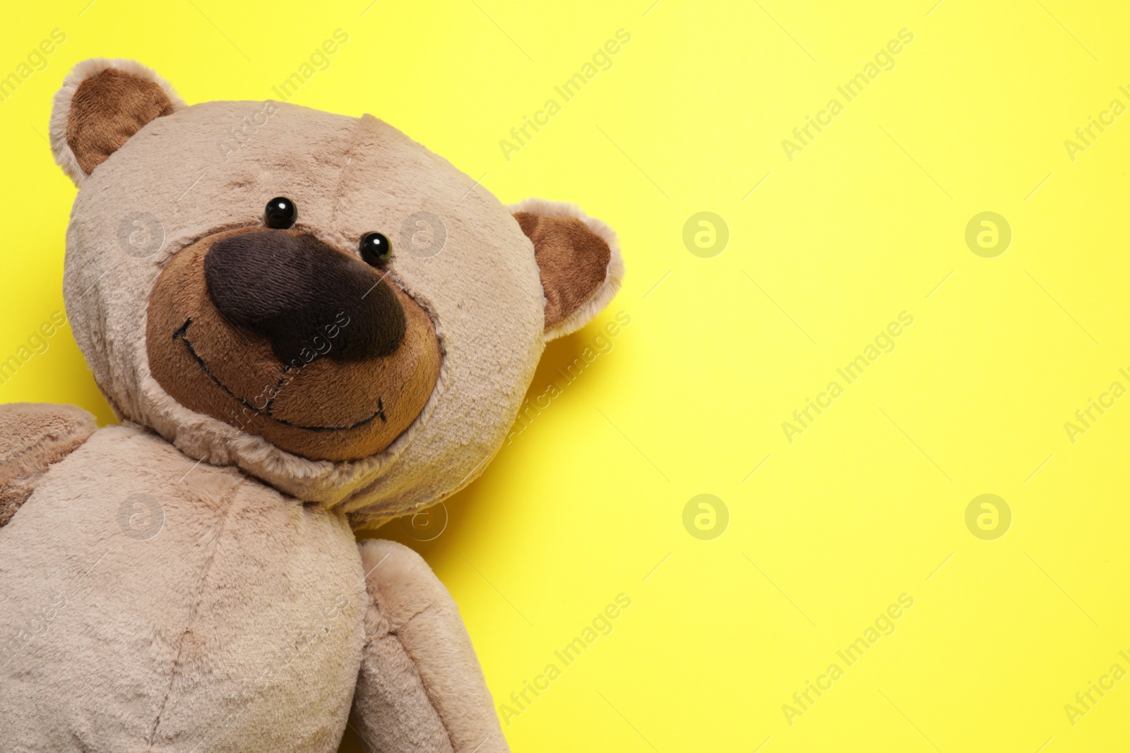 Photo of Cute teddy bear on yellow background, top view. Space for text