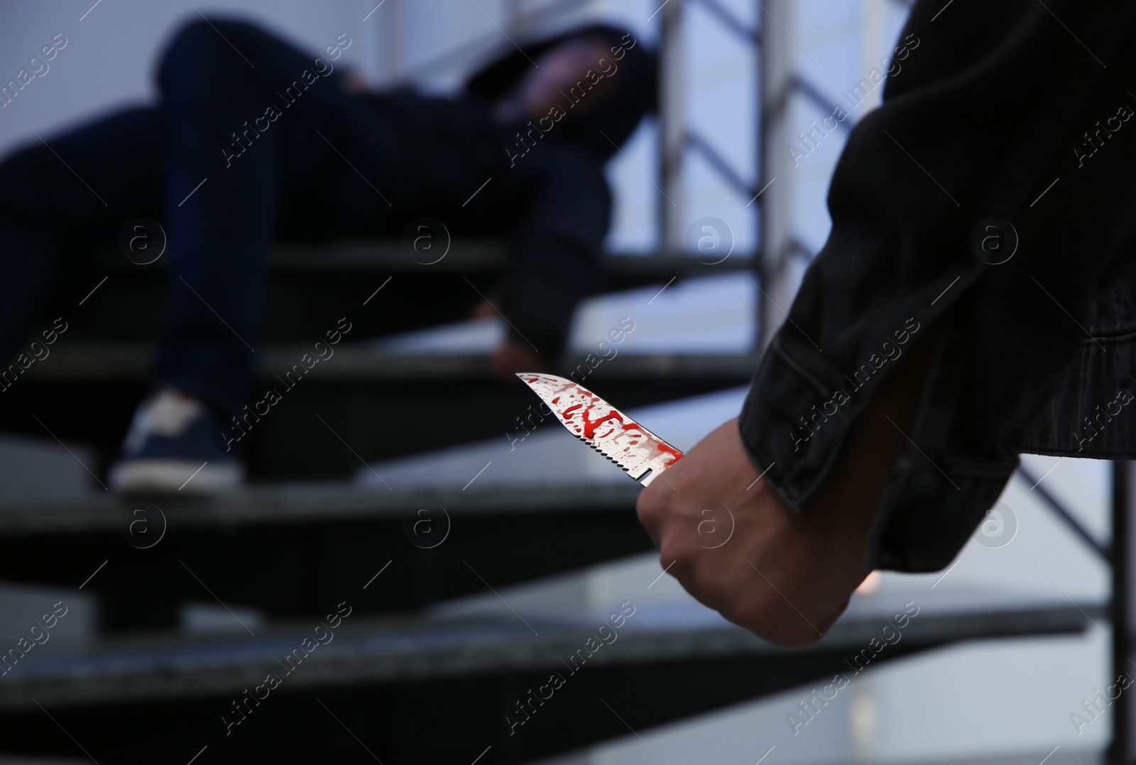 Photo of Man with bloody knife and unconscious person on stairs indoors, space for text. Dangerous criminal