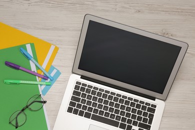 Modern laptop, glasses and office stationery on white wooden table, flat lay. Distance learning