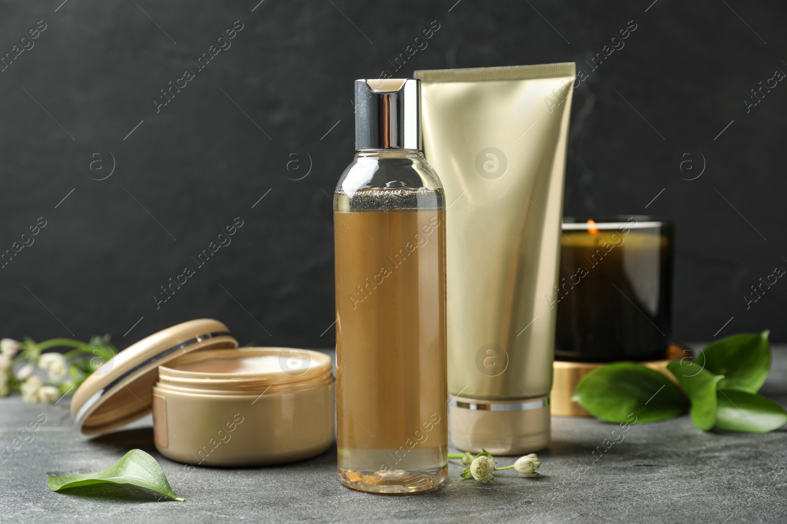 Photo of Cosmetic products and burning candle on grey stone table