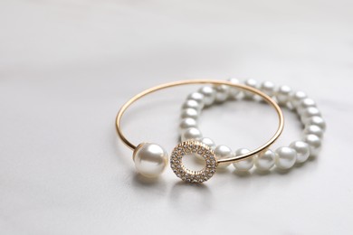 Elegant bracelets with pearls on white marble table, closeup