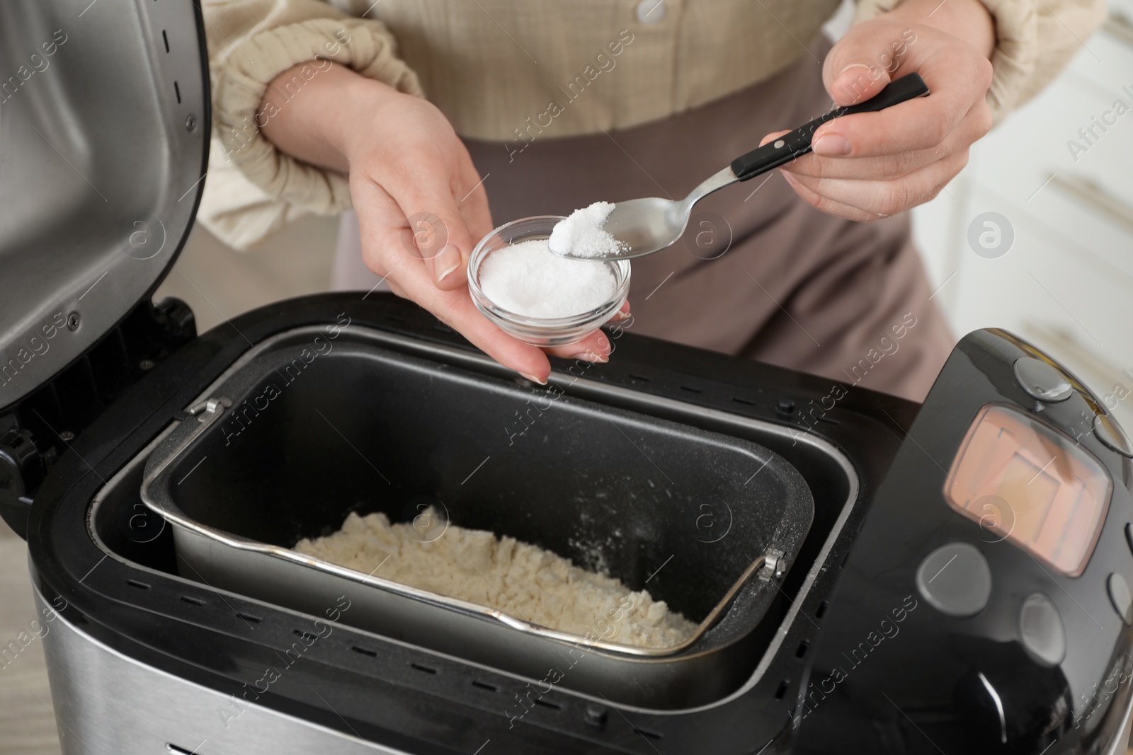 Photo of Making dough. Woman adding salt into breadmaker machine, closeup