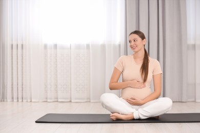 Photo of Pregnant woman sitting on yoga mat at home, space for text