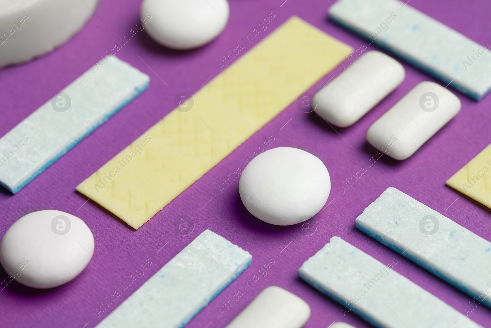 Photo of Different tasty colorful bubble gums on purple background, closeup