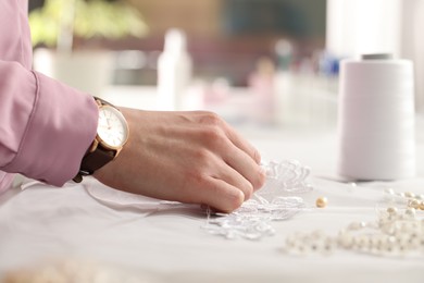 Photo of Dressmaker working with beautiful white lace at table in atelier, closeup