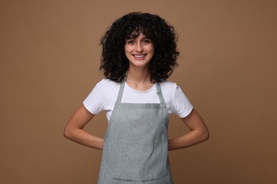 Photo of Happy woman wearing kitchen apron on brown background. Mockup for design