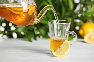 Pouring hot lemon tea into glass cup on white table