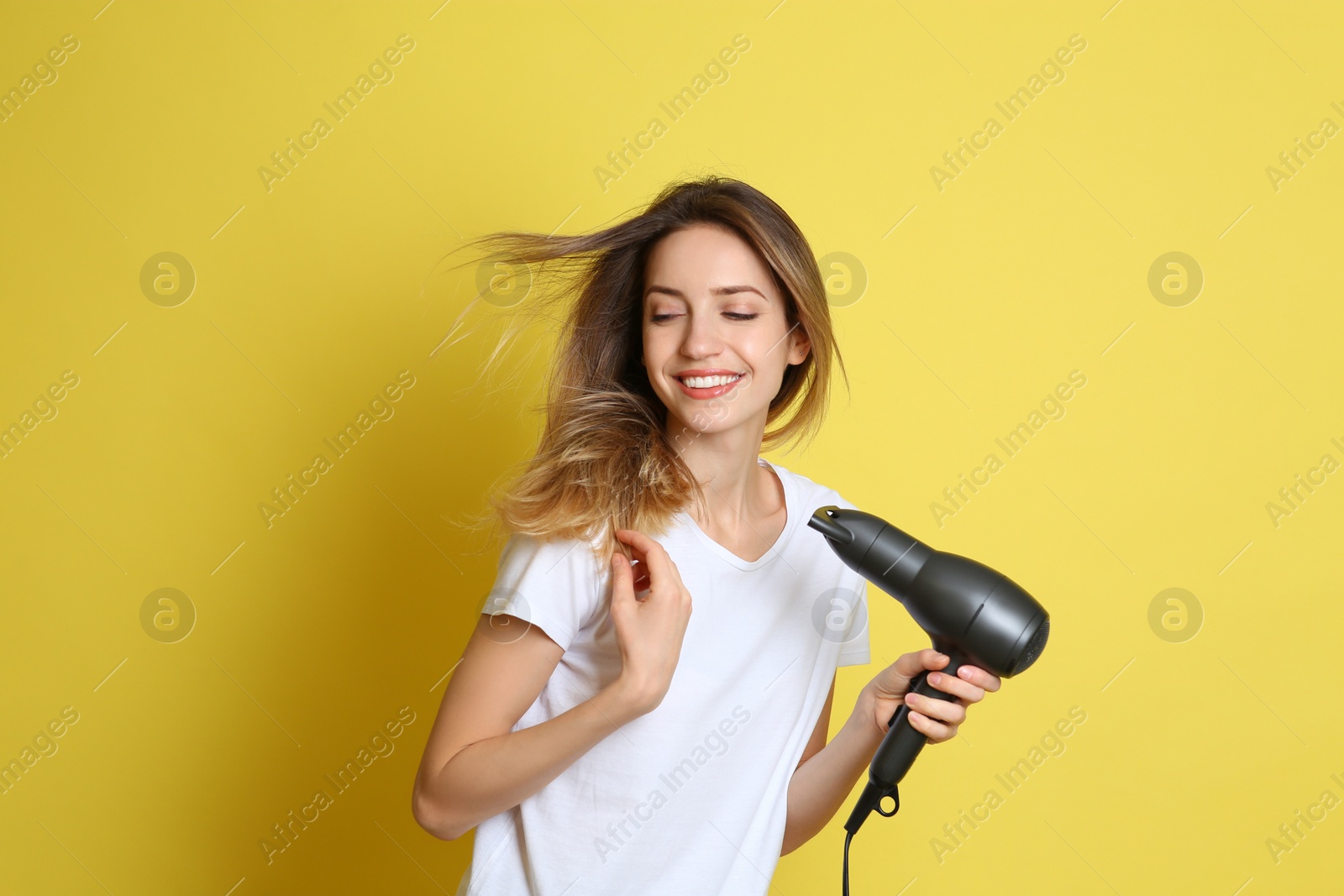 Photo of Beautiful young woman using hair dryer on yellow background