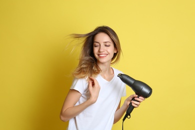 Beautiful young woman using hair dryer on yellow background