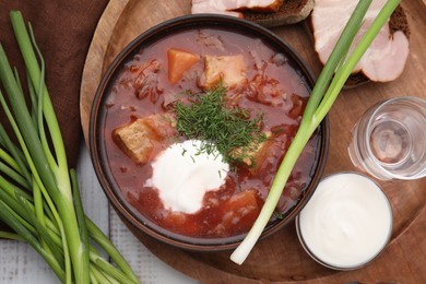 Tasty borscht with sour cream in bowl served on white wooden table, flat lay