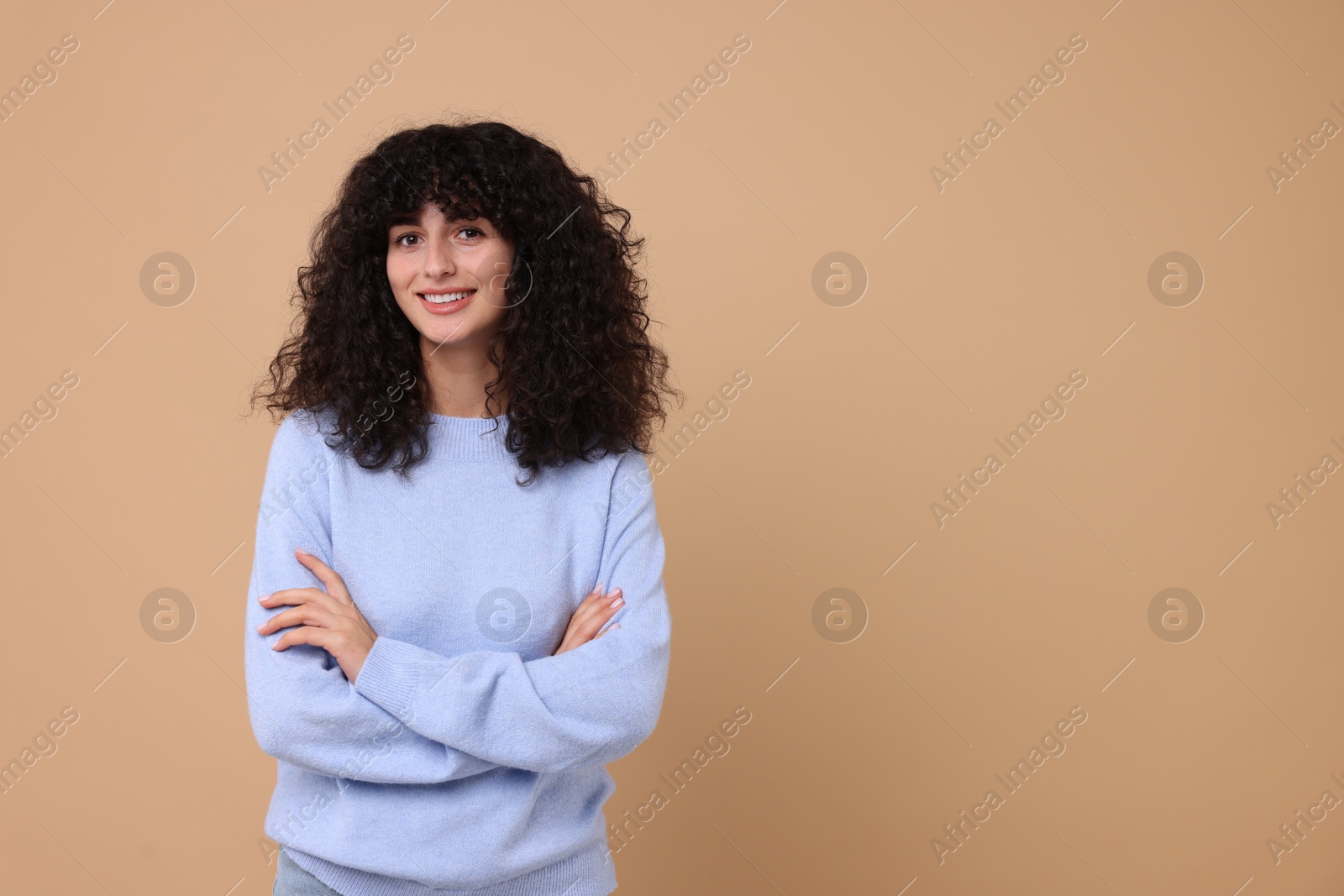 Photo of Happy young woman in stylish light blue sweater on beige background, space for text