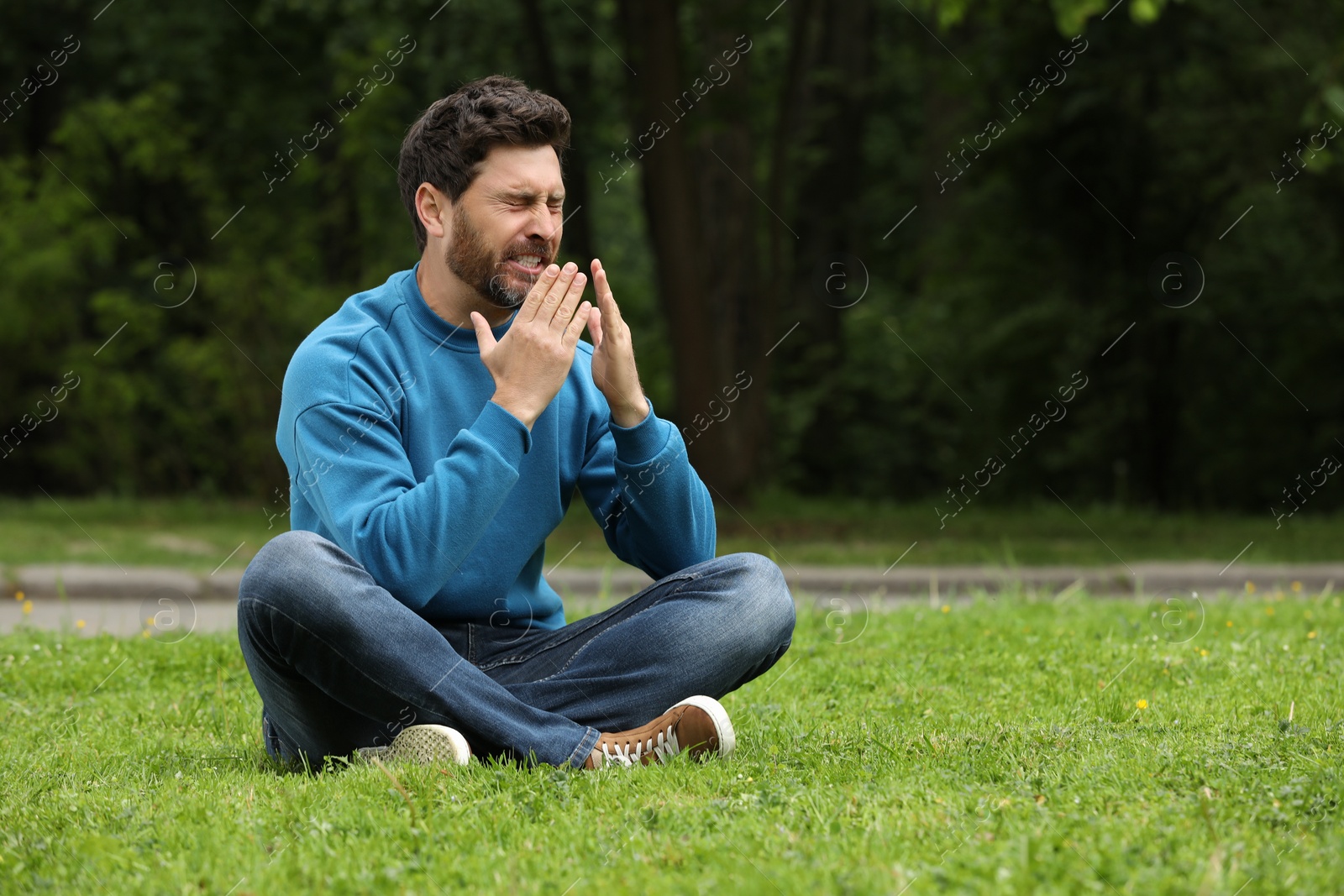 Photo of Man suffering from seasonal spring allergy on green grass in park. Space for text