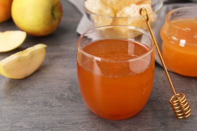 Glass of honey, apples and dipper on dark table