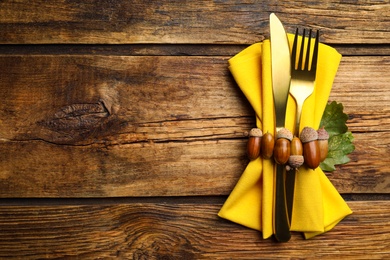 Photo of Seasonal table setting with autumn decorations on wooden background. Cutlery with acorns and space for text, top view