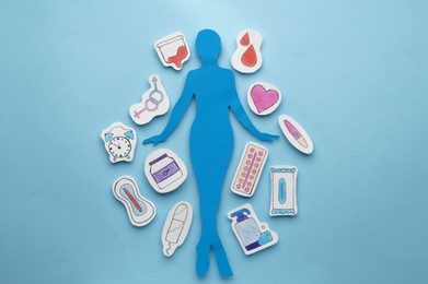 Photo of Woman paper figure with personal hygiene products and gender sign on light blue background, flat lay
