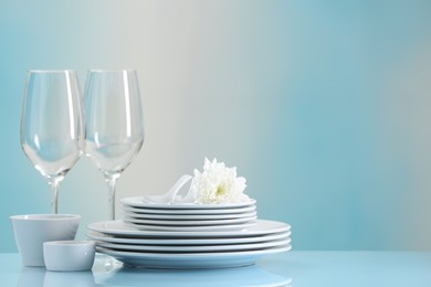 Photo of Set of many clean dishware, flower and glasses on light blue table. Space for text