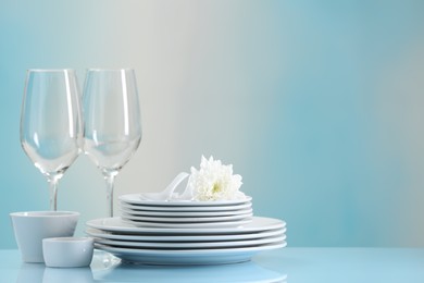 Set of many clean dishware, flower and glasses on light blue table. Space for text